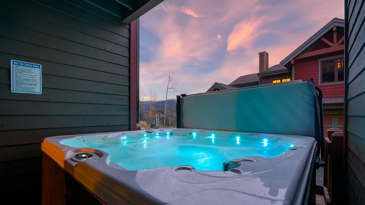 A serene exterior shot featuring a private hot tub with a clear view of the sky and surrounding architecture. The image evokes a sense of relaxation and luxury, suggesting the experience of soaking while watching the sunset or mountains after a day of adventure.