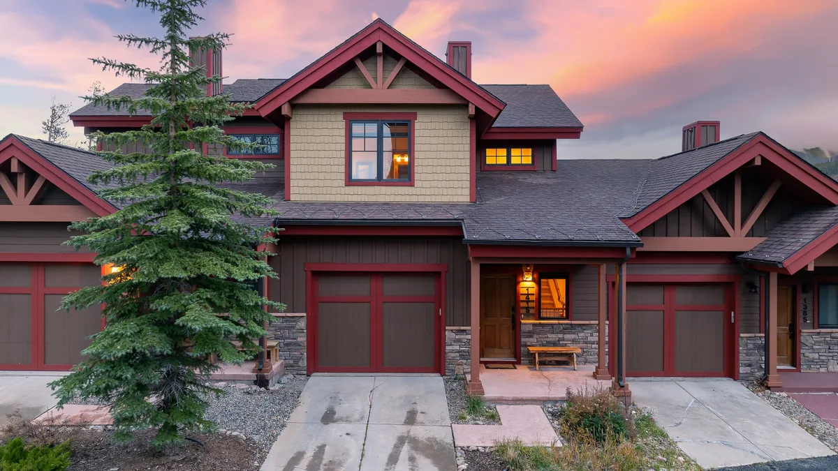 A welcoming exterior shot of Chalet 1415’s front entrance framed by landscaped paths and a sunset sky, showcasing the home's impressive architecture and inviting ambiance. The garage doors and open porch hint at space for gatherings and outdoor enjoyment.