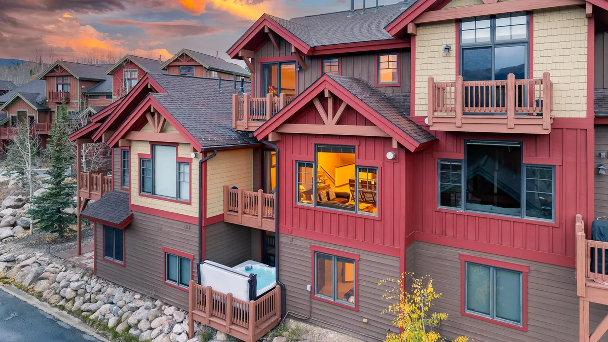 An inviting exterior shot of the chalet, featuring warm light glowing from the windows, detailed architectural features, and surrounding natural elements. The balcony and cozy ambiance suggest a welcoming space for evening gatherings or enjoying the fresh mountain air.