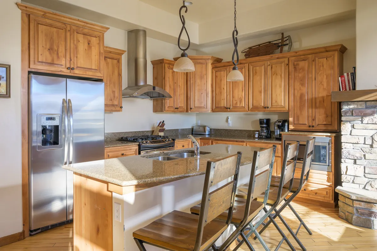 This image features a spacious, well-equipped kitchen with a large island, stainless steel appliances, wooden cabinetry, and granite countertops. The kitchen looks ready for meal preparation and social gatherings, with ample space for cooking and entertaining.