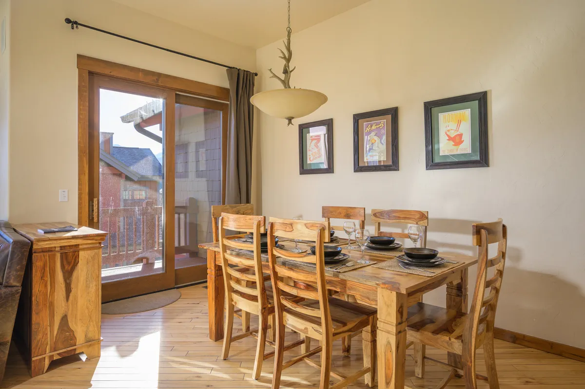 A bright dining area with a central table, sliding glass door providing natural light, and tasteful wall art. The space is arranged for family dinners and comfortable gatherings, with a clear connection to the kitchen area.
