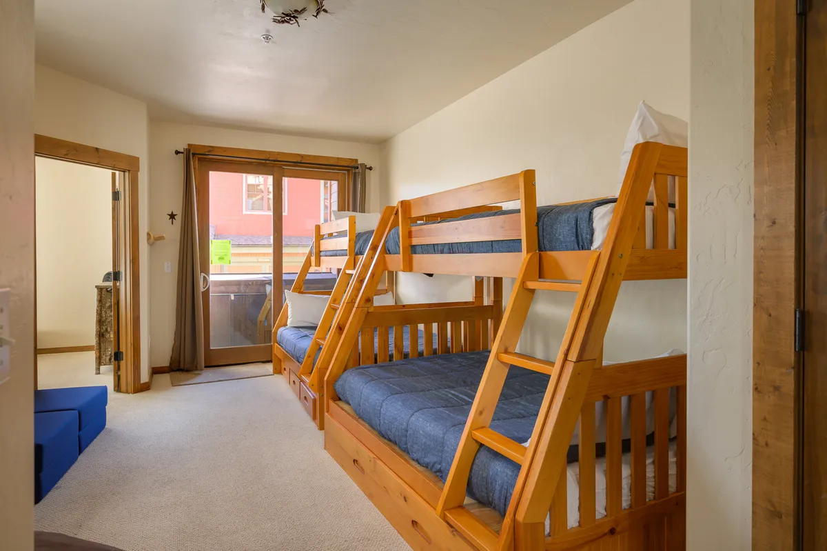 A bright bunk room with inviting twin bunk beds, textured walls, and a sliding glass door that lets in natural light. The space feels playful yet cozy, ideal for children, cousins, or friends.