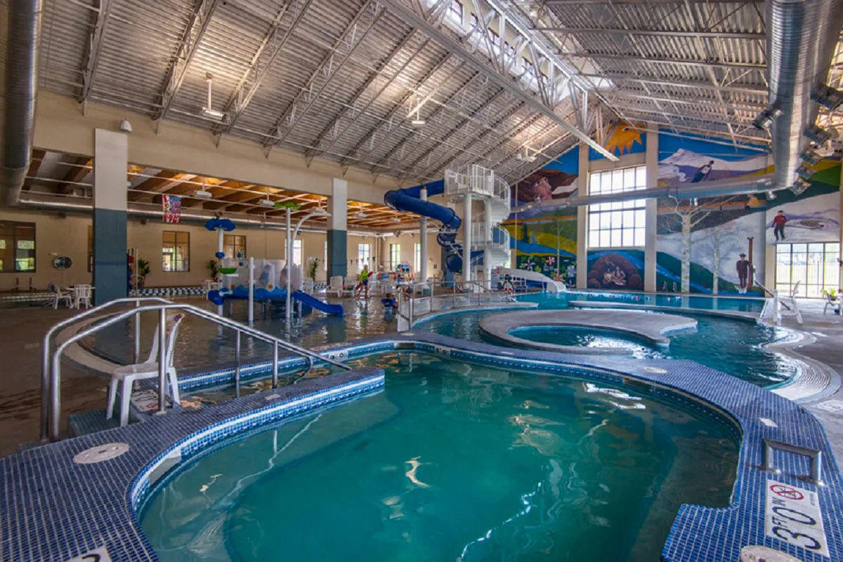 This image captures a vibrant pool area with a thrilling water slide, a colorful mural on the wall, and children joyfully playing in the water. The scene is full of energy and laughter, clearly illustrating a family-friendly space for fun and bonding.