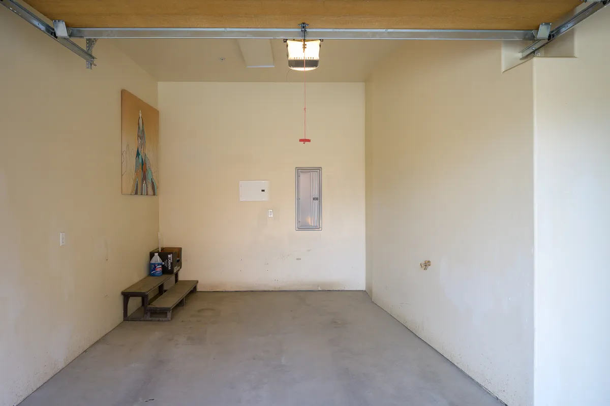 A functional interior garage space with visible artwork, bench seating, and an electrical panel. The tidy and utilitarian design suggests practical storage and organization, with space for parking and gear.